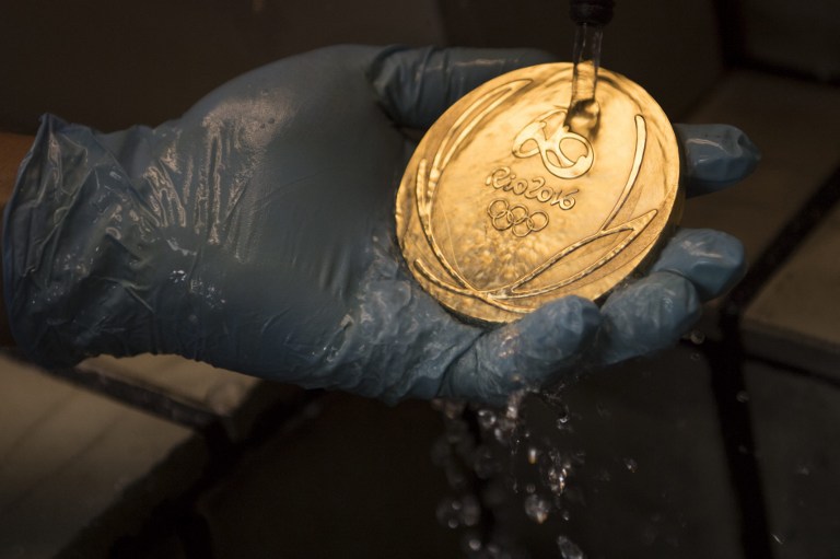 A worker cleans a gold medal for the Rio Olympic Games after its gold bath at a coin factory in Rio de Janeiro, Brazil, on July 18, 2016. / AFP PHOTO / CHRISTOPHE SIMON