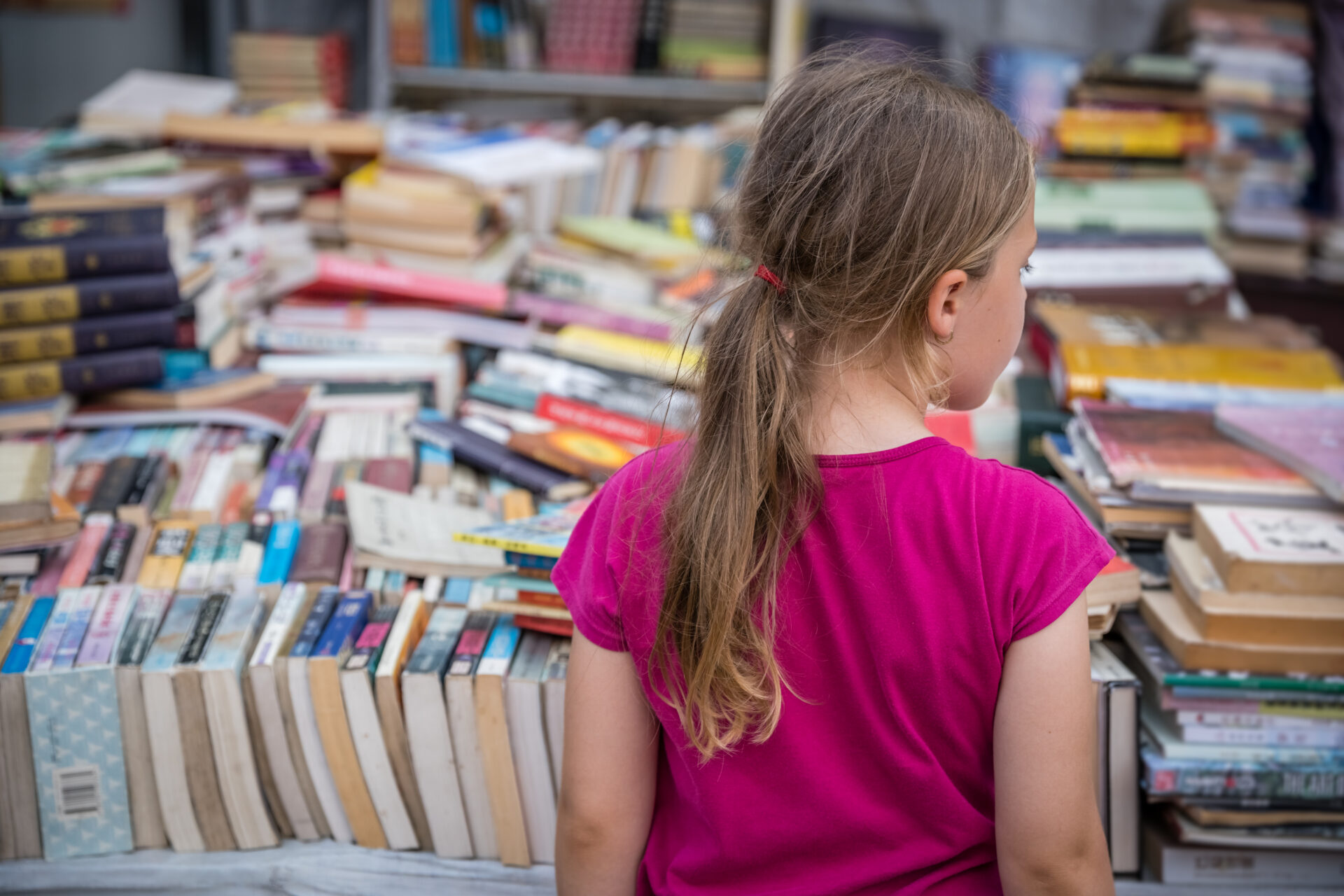 Chengdu, China - July 2019 : Young Caucasian girl looking at the pile of second hand books for sale on a street market